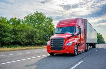 Red big rig long haul semi truck with black grille transporting cargo in dry van semi trailer...