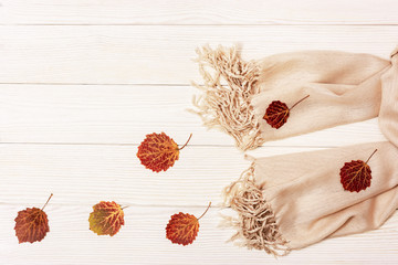 Autumn flat lay, red autumnal season leaves of aspen tree, fabric scarf on light wooden table with copy space. View from above.