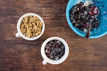 Blue bowl of with blackberries in sugar/flour mix, white bowls with blackberry crumble dessert, on...
