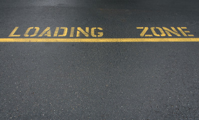 Yellow line and loading zone text on an asphalt street
