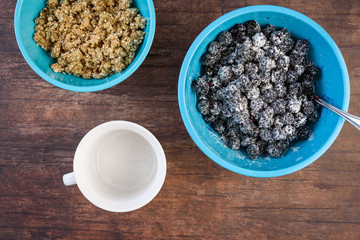 Blue bowls of crumble topping and blackberries in sugar/flour mix, empty white bowl, on a wood background
