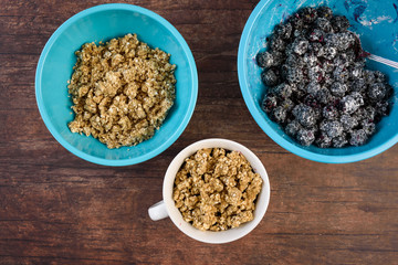 Blue bowls of crumble topping and blackberries in sugar/flour mix, white bowl, on a wood background
