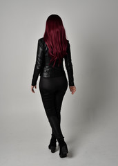 Full length portrait of  girl with red hair wearing black leather jacket, pants and boots. Standing...
