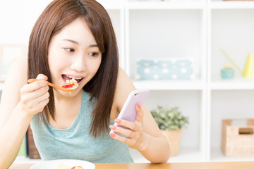 朝食を食べながらスマホを見る女性