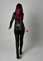 Full length portrait of  girl with red hair wearing black leather jacket, pants and boots. Standing...