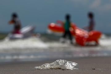 Single use plastic bag washed up on the beach as beach goers enter the water