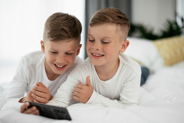 Fototapeta premium Two little brothers are playing games on the phone. Beautiful boys enjoying at home...