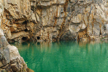 A green-colored lake and a rocky cliff with holes in abandoned adits. Tuim is a sinkhole at the site of an abandoned copper and tungsten ore mine.
