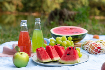 Outdoor summer lifestyle with a picnic laid out in a meadow with delicious summer fruits, watermelon and refreshing drinks on a blanket. Picnic time.