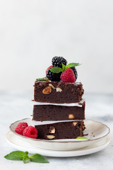 pieces of fresh chocolate brownie with hazelnuts, raspberries and blackberries. Bakery, confectionery concept. Gray background. vertical image
