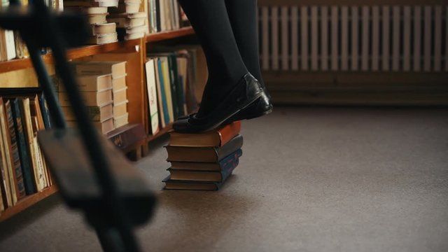 Legs of girl that stands on the books trying to reach upper shelves in the library.