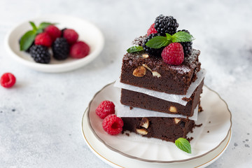close-up of delicious chocolate brownie square pieces with hazelnuts, decorated with raspberries and blackberries. traditional homemade dessert. Gray background. copy space.