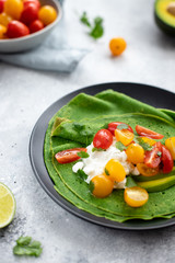 crepes with spinach, avocado, cottage cheese and colorful cherry tomatoes on a gray concrete background. diet concept. vertical image, selective focus