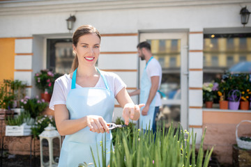 Brown-haired female with ponytail cutting leaves, bearded male standing outside flower shop