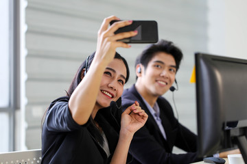 Asia Beautiful woman customer support operator taking a selfie photo of her team  in a call center
