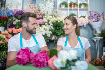 Bearded male and brown-haired female in aprons arranging flowers, looking at each other