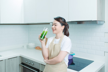 Happy smiling asian girl with glass of healthy fresh raw vegetable smoothie at home.