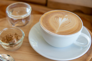 a white cup of hot latte with a glass of water and a glass of sugar.