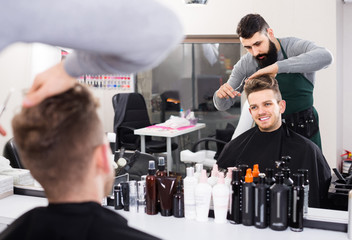 adult english male hairdresser doing haircut for male client at hair salon.