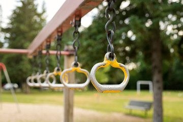 Playground in the park. Metal monkey bars on chains. Playground for children in the local park with field and trees in the background. 