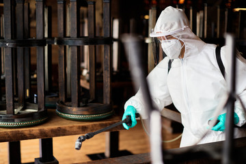 Disinfection worker in hazmat suit spraying contaminated cafe due to coronavirus epidemic.