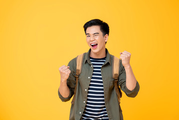 Portrait of happy excited  young Asian tourist backpacker man raising his fists doing success...