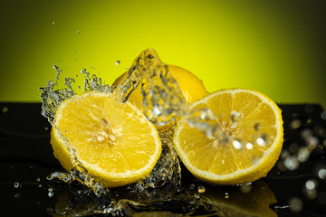 Fototapeta na wymiar two halves of lemon next to one whole with a stream and splash of water on a yellow background