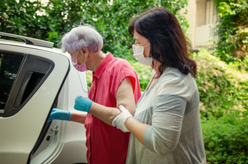 Caregiver as a medical escort to accompany an elderly client to the hospital. Both wear protective...