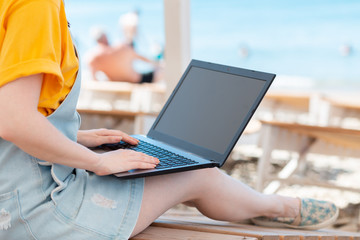 A person uses a laptop. In the background, the sea and the beach. The concept of freelancing and studying