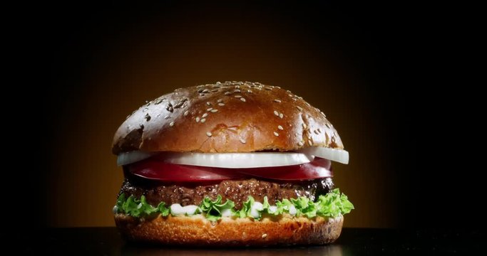 Yummy juicy burger with fresh ingredients rotating in front of camera. Delicious hamburger with grilled beef steak served on chef's table 4k footage close up shot