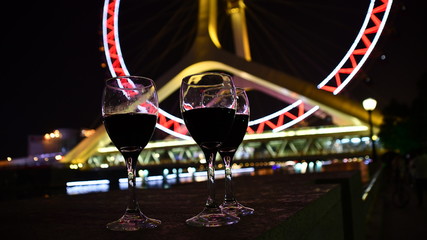three glasses with wine with ferry's wheel at the background at night from the low angle