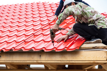 Workers install red metal tiles on the roof