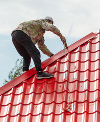 Workers install red metal tiles on the roof