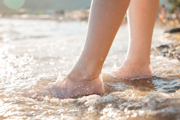 A woman stands in rubber shoes for swimming on the beach. Feet in the water close-up. The concept of the protection and health of the feet