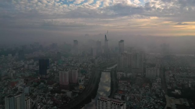 sunrise drone shot tracking over high-rise apartment buildings and canal looking to City skyline of Ho Chi Minh City with heavy fog and low clouds obscuring building