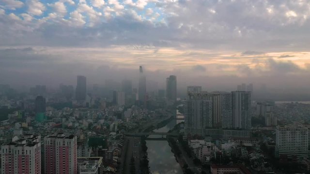sunrise drone shot flying in towards high-rise apartment buildings and canal looking to City skyline of Ho Chi Minh City with beautiful color heavy fog and low clouds obscuring buildings