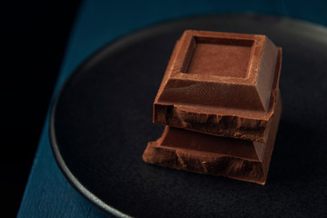 Two pieces of chocolate in black plate on the edge of blue wooden table