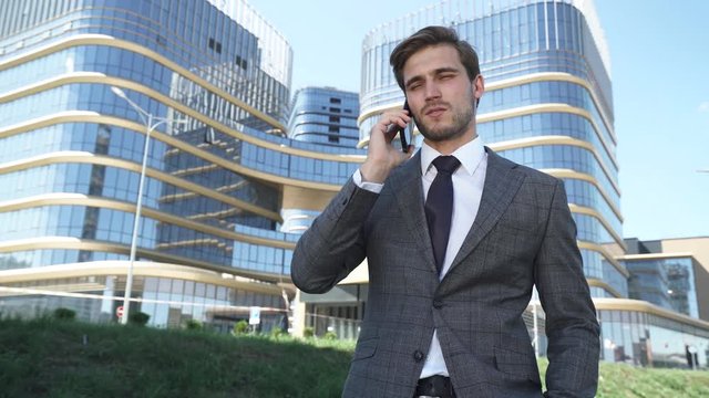 Businessman, top manager in a suit stands near a glass skyscraper and talking on a mobile phone, young businessman manager near the modern office.