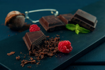 Pieces of chocolate, chocolate shavings, raspberry, mint and strainer with cocoa on dark wooden...
