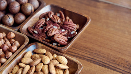 Wooden bowl with mixed nuts on table top view. Healthy food and snack. Walnut, pistachios, almonds, hazelnuts and cashews.