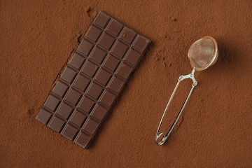 Chocolate bar and strainer on cocoa powder background.