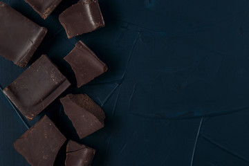 Pieces of chocolate on dark blue textured background. Flat lay. Copy space.