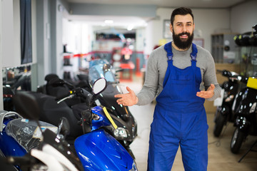 Male worker demonstrates different models of motorcycles in his workshop