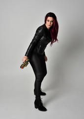 Full length portrait of  girl with red hair wearing black leather jacket, pants and boots. Standing...