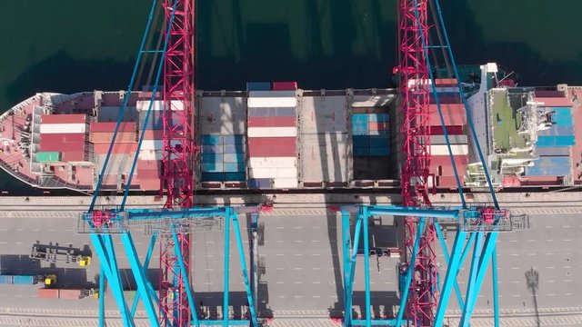 Drone flying over a container ship and ship's automatic loaders during cargo operations over the customs area in the seaport. Panorama of the container port. High quality 4k footage