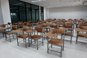 Empty school classroom with many wooden chairs. Wooden chairs in classroom. Empty classroom with vintage tone wooden chairs. Empty college classroom. Education stock photo.