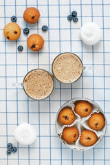 Two cups of foamy latte and muffins, blueberries, marshmallows on a checkered tablecloth. Breakfast concept. Flatlay design.