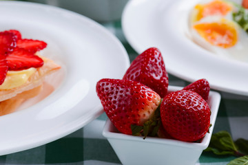 Fresh strawberries in a small white bowl served on the table with other dishes. Healthy vegan food.