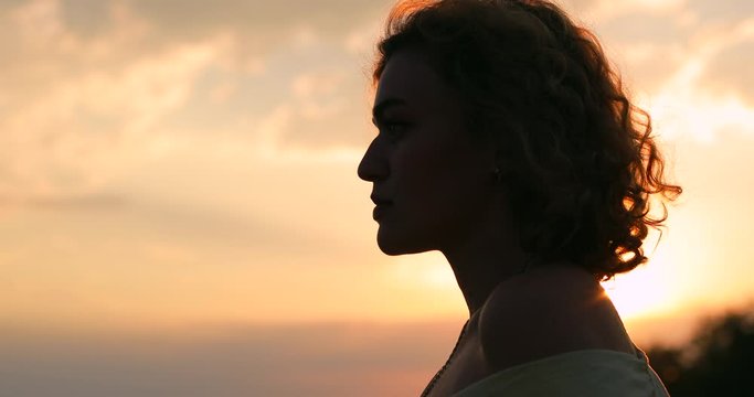 Silhouette of curly woman against orange sunset background