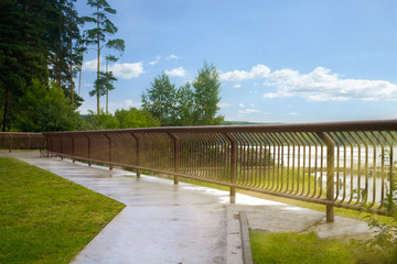 The road along the river embankment on a bright Sunny day along the metal fence. Landscape with sun rays